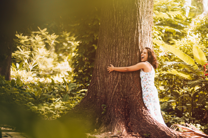 A woman hugging a large tree in a lush green forest, symbolizing appreciation for nature and environmental conservation. Perfect for articles about tree care tips.